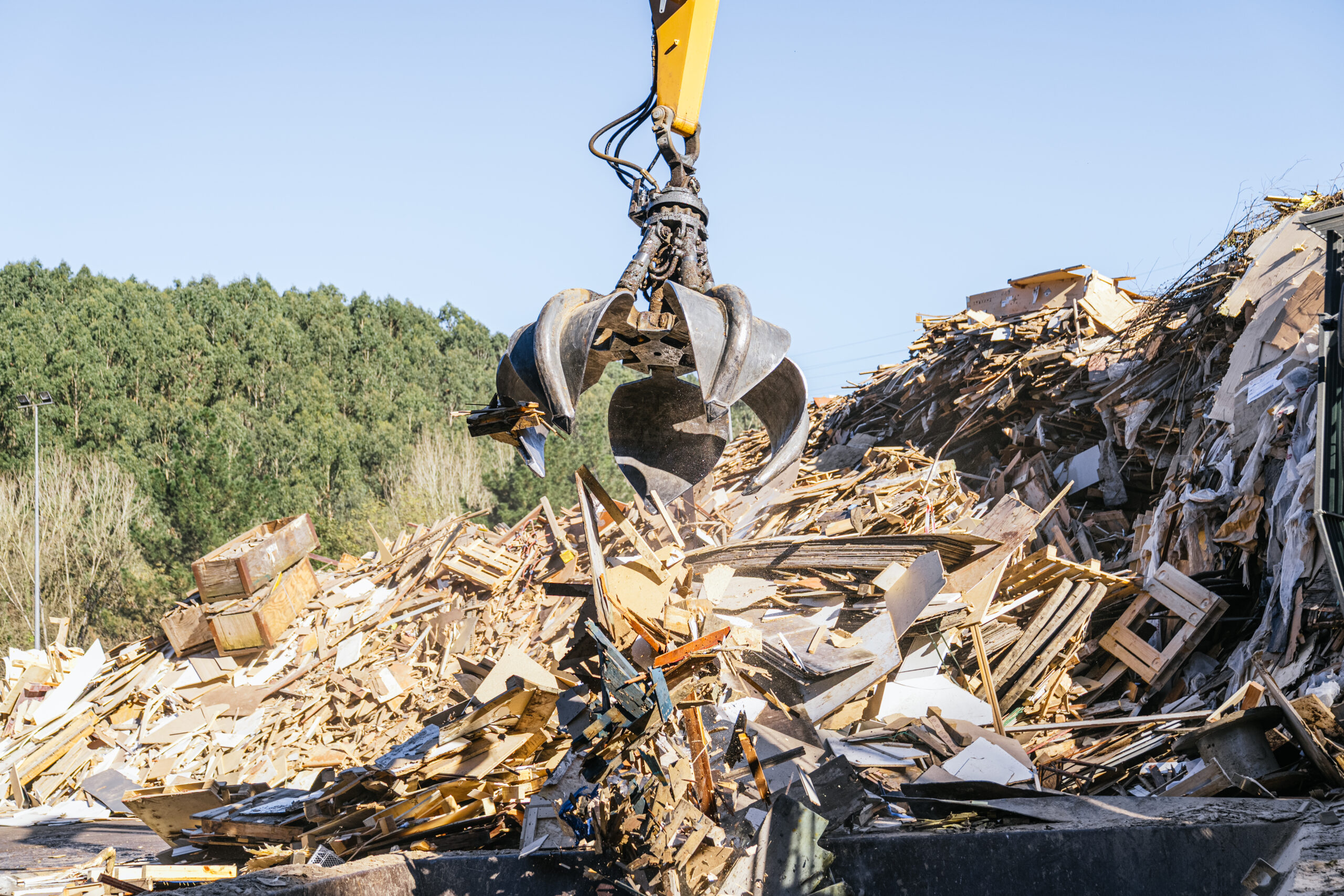 Mechanical claw sorting wood waste at a landfill on a sunny day, efficiently managing recycling efforts and promoting sustainability